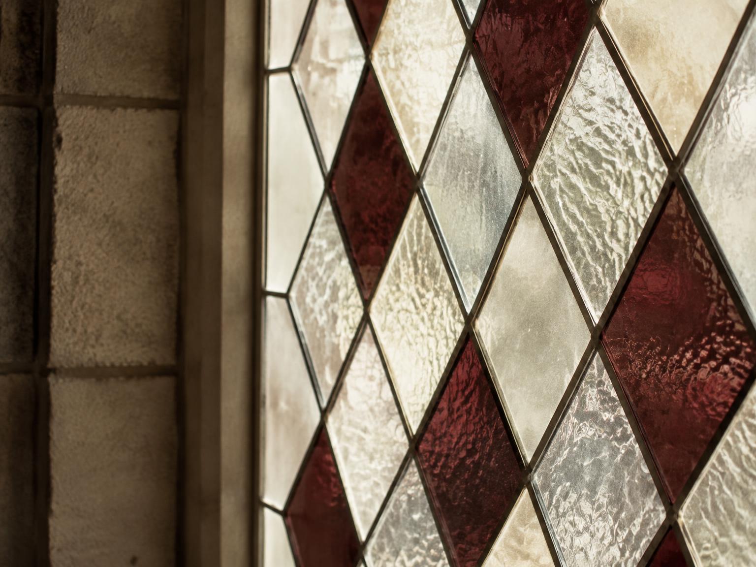 Close-up of textured clear and burgundy diamond quarries joined by fine lead cames beside a stone reveal.